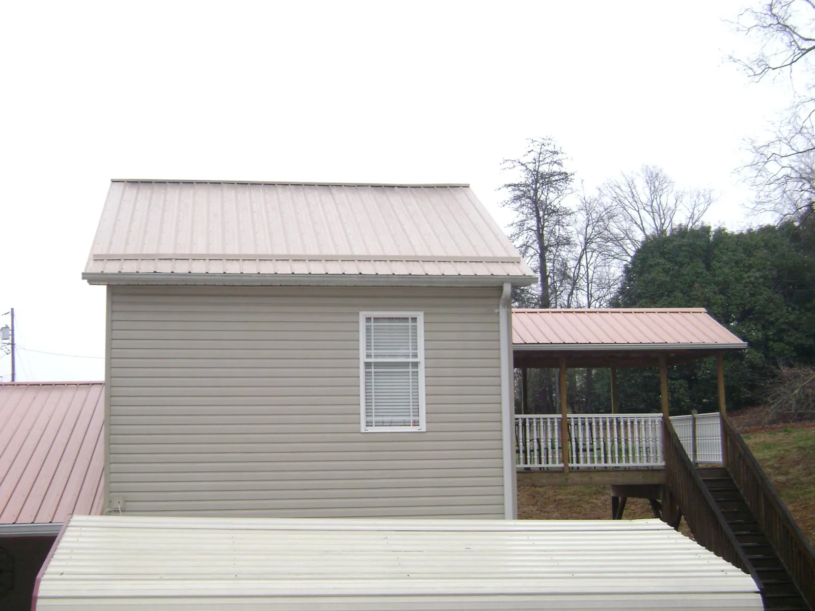 Tan metal roofs on a two story addition and attached porch, from a Roof Replacement job in Ridgeland